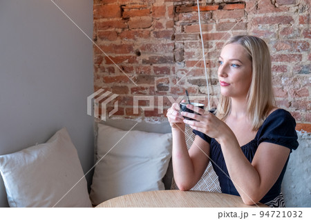 Beautiful smiling woman drinking coffee at cafe. Portrait of young blonde woman in a cafe drinking 94721032