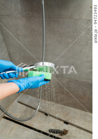 A woman cleans a shower head from limestone. 94723493