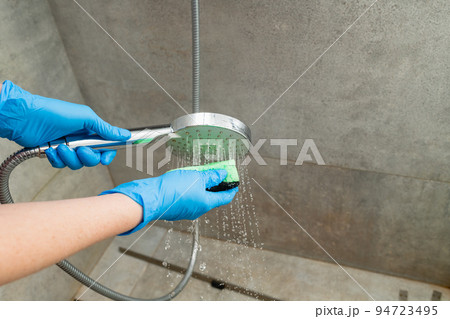 A woman cleans a shower head from limestone. 94723495
