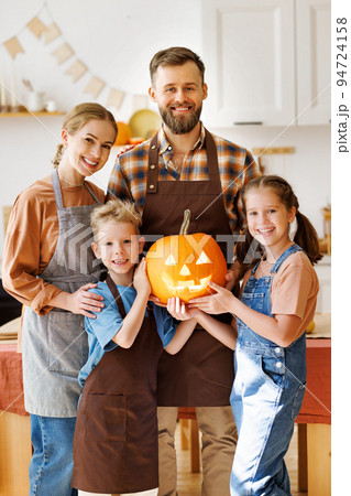 Happy family mother, father and kids smiling at camera make jack-o-lantern from pumpkin, getting ready for halloween Happy family mother, father and kids smiling at camera make jack-o-lantern from pumpkin, getting ready for halloween 94724158