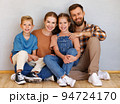 Happy family mother father and children sitting on floor against empty grey wall 94724170
