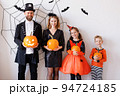 Cheerful family in carnival costumes celebrate Halloween near a gray wall with cobwebs and bats 94724185