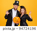 Cheerful couple in carnival costumes does scary gesture and celebrate Halloween on colored yellow background 94724196