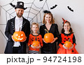 Cheerful family in carnival costumes celebrate Halloween near a gray wall with cobwebs and bats 94724198