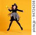 Happy girl in witch costume with pumpkin basket jumping and celebrates Halloween on yellow background 94724208