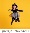Happy girl in witch costume with pumpkin basket jumping and celebrates Halloween on yellow background 94724209