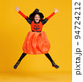 Happy ethnic girl in witch pumpkin costume jumping and celebrates Halloween on yellow background 94724212