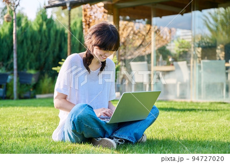 Teenage girl sitting on the grass using a laptop 94727020