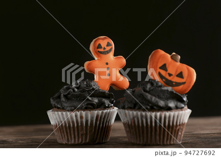 Two holiday cupcakes with halloween party decorations gingerbread man and pumpkins on black background. Close up. Two holiday cupcakes with halloween party decorations gingerbread man and pumpkins on black background. Close up. 94727692