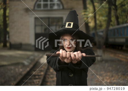 Portrait young woman in witch costume holds magic wand in front her. Halloween party. School of Magic 94728019