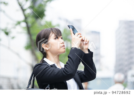 屋外でスマートフォンを使うスーツ姿の若い女性 屋外でスマートフォンを使うスーツ姿の若い女性 94728692