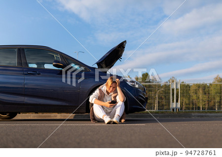 woman driver waiting for help from emergency tow truck near broken down car with open hood 94728761
