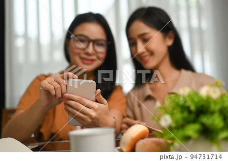 Two happy young woman using smart phone while sitting in modern coffee shop 94731714