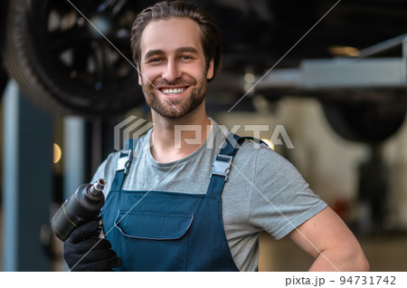 Joyful young car mechanic holding a work tool 94731742