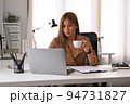 Beautiful young businesswoman drinking coffee and checking online information on laptop 94731827