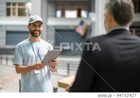 A courrier in a cap giving a box to the man in a suuit 94732427
