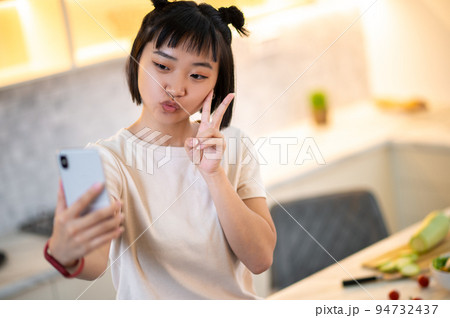 Young woman photographing herself on the smartphone in the kitchen 94732437