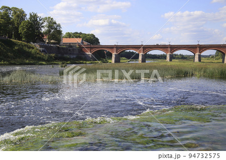 View from the waterfall to the ancient arched brick bridge and old city. High quality photo 94732575