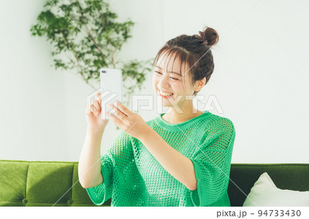 ソファに座ってスマホを見る女性 94733430