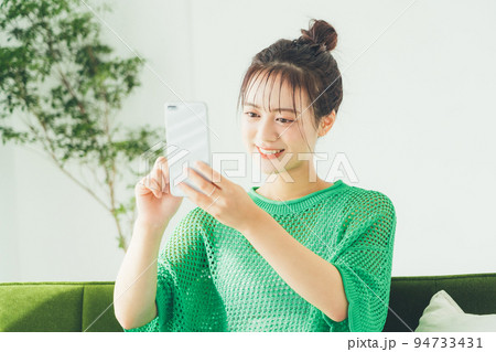 ソファに座ってスマホを見る女性 94733431