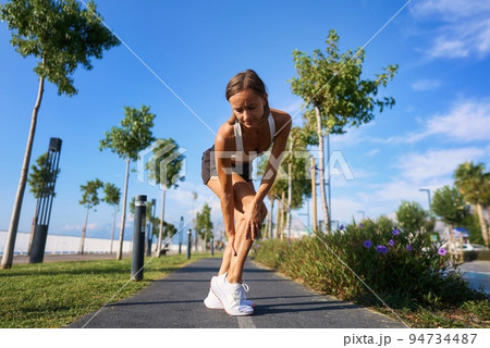 Caucasian female runner sport woman has leg cramp while she is running on beach in morning 94734487