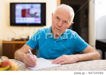Concentrated elderly man filling up papers at home table Concentrated elderly man filling up papers at home table 94734560