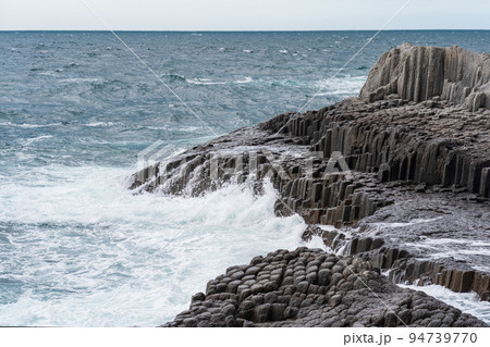 rocky seashore formed by columnar basalt against the backdrop of a stormy sea, coastal landscape of the Kuril Islands rocky seashore formed by columnar basalt against the backdrop of a stormy sea, coastal landscape of the Kuril Islands 94739770