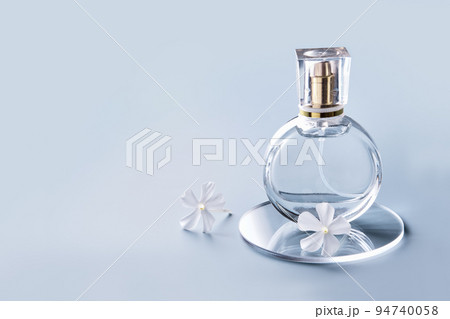 Glass perfume bottle, white flowers and round slides on blue background. Winter or spring floral fragrance Glass perfume bottle, white flowers and round slides on blue background. Winter or spring floral fragrance 94740058