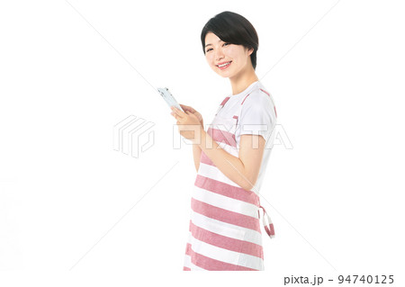 スマホを操作するエプロン姿の若い主婦(白バック) スマホを操作するエプロン姿の若い主婦(白バック) 94740125