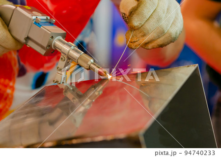 Welder hands using handheld laser welding machine - close up 94740233