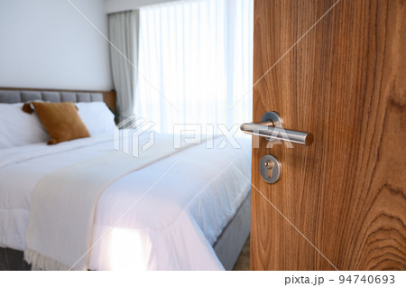 wooden door open to modern bedroom. selective focus to door handle, bedroom blurred on background. Hotel room, Condominium, or apartment doorway. 94740693
