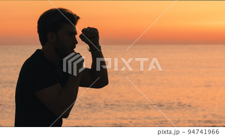 Silhouette of a boy throwing punches at dawn on the beach 94741966
