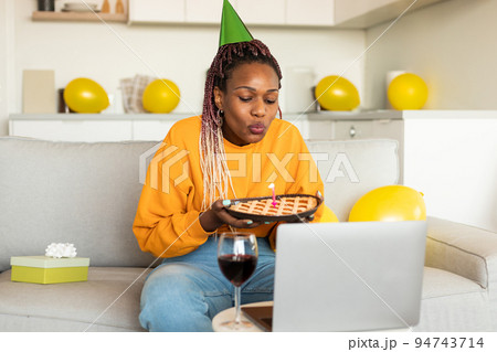 African american birthday lady blowing candle on pie, video calling via laptop and celebrating b-day remotely African american birthday lady blowing candle on pie, video calling via laptop and celebrating b-day remotely 94743714