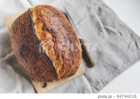 Round fresh bread lies on the cutting board. Baking and confectionery in a bakery or restaurant. Round fresh bread lies on the cutting board. Baking and confectionery in a bakery or restaurant. 94744219