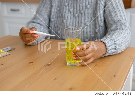 African American woman with a cold measures her body temperature and drinks soluble pills or vitamins, A tired sick woman 94744242