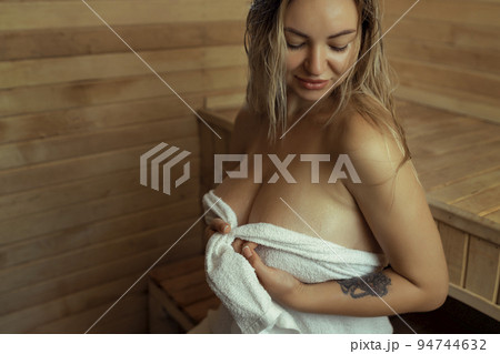 A young woman relaxes and sweats in a hot sauna wrapped in a towel. girl in the sauna. Finnish sauna interior, classic wooden sauna with hot steam. Russian bath. A young woman relaxes and sweats in a hot sauna wrapped in a towel. girl in the sauna. Finnish sauna interior, classic wooden sauna with hot steam. Russian bath. 94744632