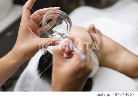 Close-up shot of a woman getting facial treatment with clay mask. Cosmetology and spa 94744657