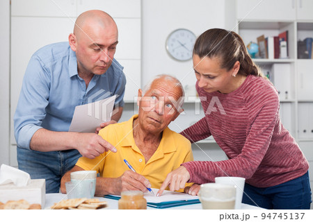 Man at table in home kitchen filling up documents with family Man at table in home kitchen filling up documents with family 94745137