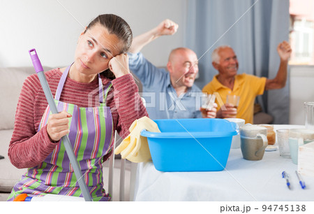 Woman sitting while cleaning house, husband and father watching tv Woman sitting while cleaning house, husband and father watching tv 94745138