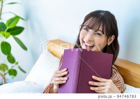 ベッドで本を読む眼鏡の若い女性 ベッドで本を読む眼鏡の若い女性 94746783