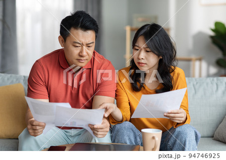 Upset asian couple checking bills, home interior Upset asian couple checking bills, home interior 94746925