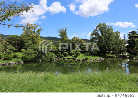 緑地と池と緑の植物のある庭園と山と青空と白い雲の見える風景 94746965