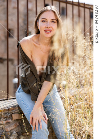 Woman in unbuttoned blouse posing near fence 94748297