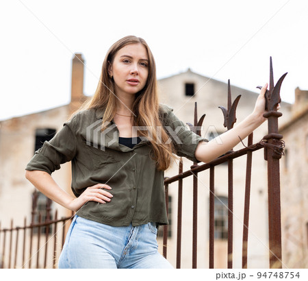 Woman posing near fence against abandoned building Woman posing near fence against abandoned building 94748754