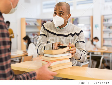 Man in mask returning books at library 94748816