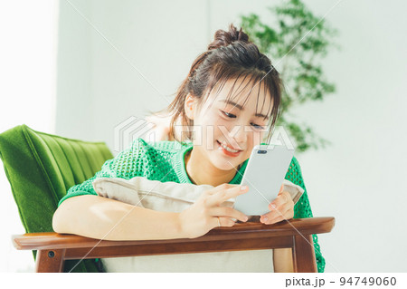 ソファに寝転がってスマホを見る女性 94749060