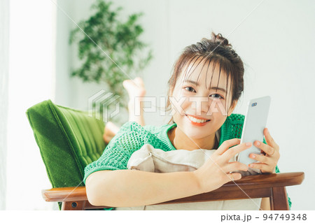ソファに寝転がってスマホを見る女性 94749348