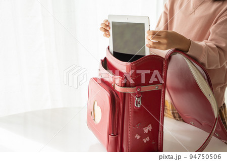 ランドセルからタブレット端末を取り出す小学生 94750506