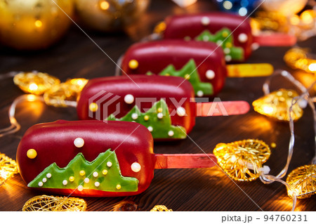 Red Christmas dessert in the form of mousse on a stick decorated with Christmas tree on a background of glowing garlands 94760231