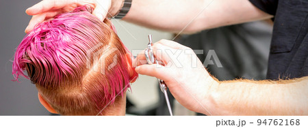 Haircut of dyed short pink wet hair of young caucasian woman by a male hairdresser in a barbershop 94762168